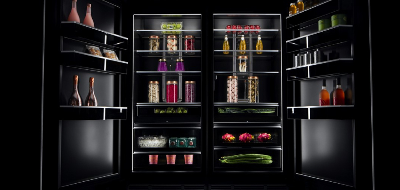 An opened JennAir Double-Door Refrigerator. On the interior door shelves on the left are champagne bottles, two other beverage bottles and two other items.  On the middle shelves are produce and jars of various foods and beverages. In the crispers are dragon fruit, Brussels sprouts and other items.  On the interior door shelves on the right are wine bottles, silver containers and green containers.